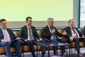Czterech mężczyzn w garniturach siedzi na fotelach w trakcie debaty.