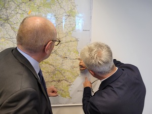 Po lewej stronie stoi Josef Doppelbauer, Dyrektor Wykonawczy Agencji Kolejowej Unii Europejskiej po prawej stronie stoi Prezes Urzędu Transportu Kolejowego dr inż. Ignacy Góra. Oglądający mapę Polski z wyznaczonymi trasami kolejowymi wiszącą na ścianie.