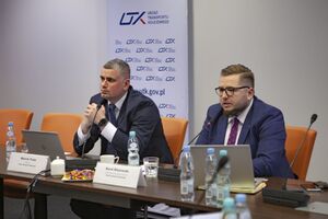Od lewej Wiceprezes UTK Marcin Trela oraz Karol Kłosowski, Dyrektor Departamentu Przewozów Pasażerskich. Mężczyźni siedzą przy stole, przed nimi komputery i mikrofony.