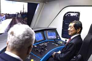 Ambasador Japonii w Polsce Miyajima Akio siedzi na fotelu maszynisty w kabinie symulatora w Centrum Egzaminowania i Monitorowania Maszynistów. Przed Ambasadorem pulpit lokomotywy, ekrany systemowe. Za szybą lokomotywy widok na tory kolejowe wyświetlane przez monitor. Na zdjęciu także Ignacy Góra - Prezes UTK.